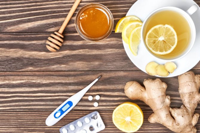 Чашка имбирного чая, мед, лимон, термометр и таблетки на деревянном фоне
