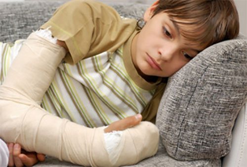 Sad boy with a plastered arm lying on the sofa